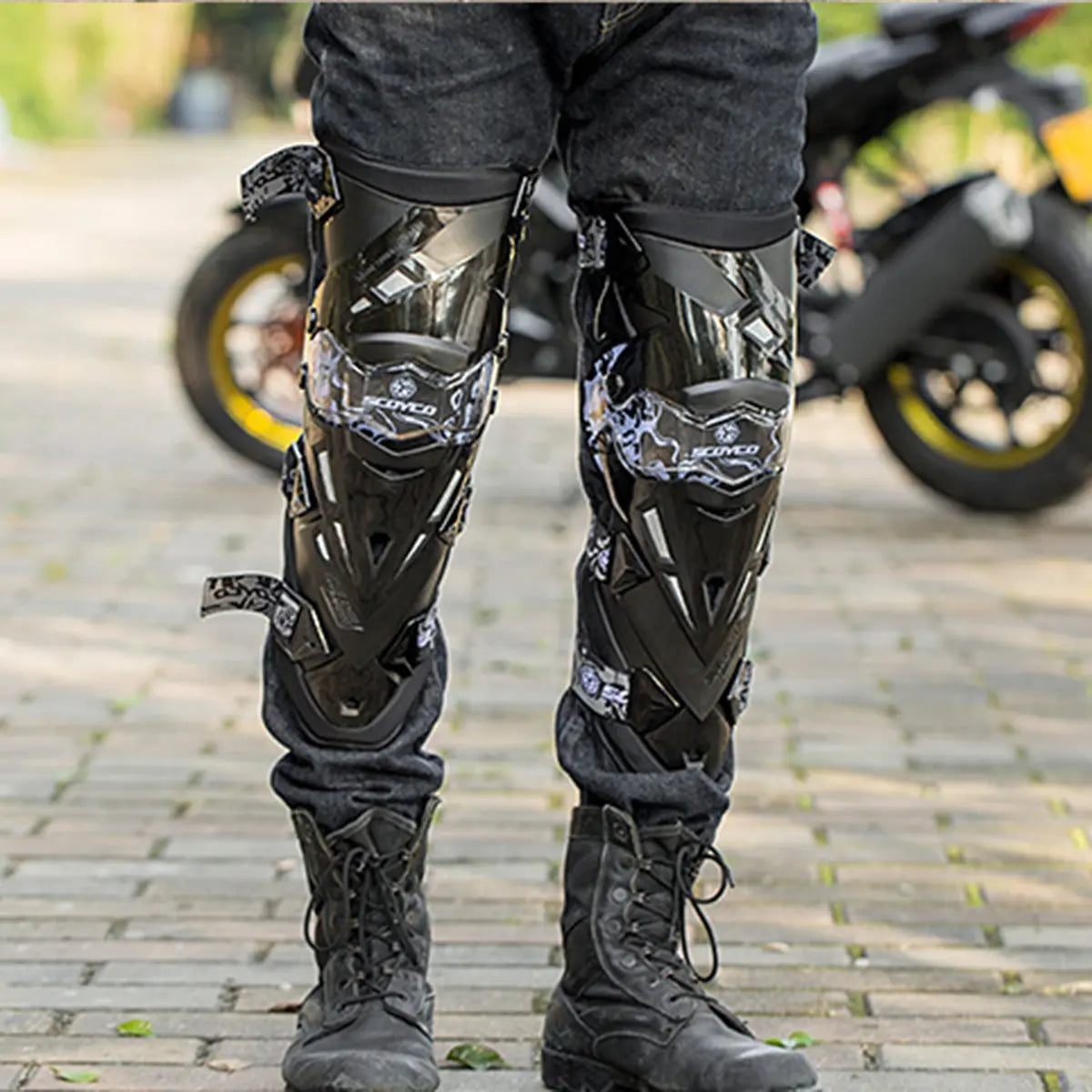 Motociclista de pie con las rodilleras Scoyco K12 puestas sobre el pantalón y botas